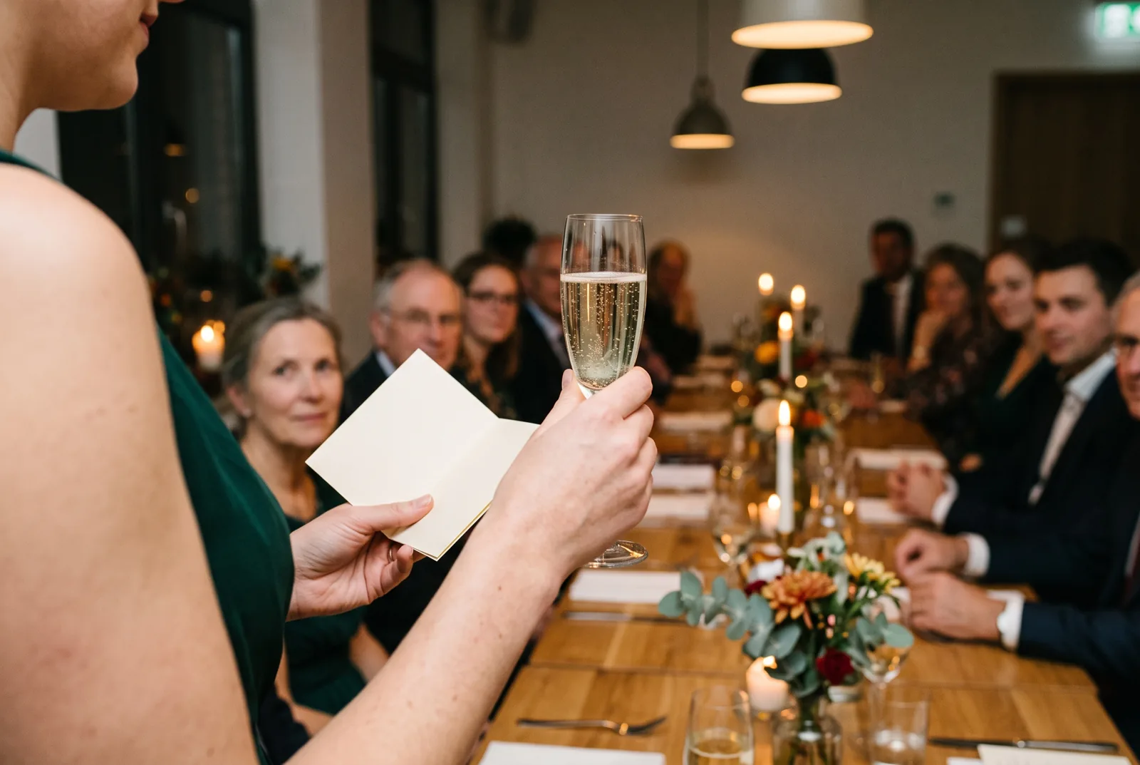Die Rednerin hebt ihr Glas, in der anderen Hand ihr Redekärtchen, die Familie hört am Tisch zu